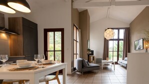 Amplia sala de estar con una mesa de comedor lista para dos personas, un sofá gris y un gran ventanal que proporciona luz natural.