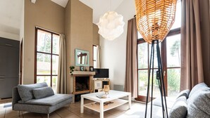 Una sala de estar con chimenea, dos sofás grises, una mesa de centro blanca y un ventanal con cortinas.