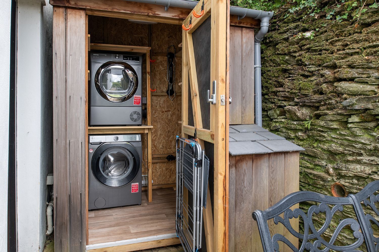 A laundry room with two washing machines, a wooden cabinet, and a stone wall.