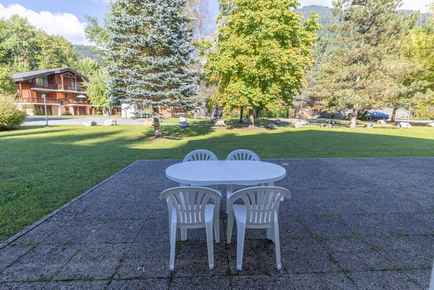 A patio with a round table and four chairs, surrounded by a well-maintained lawn and trees.