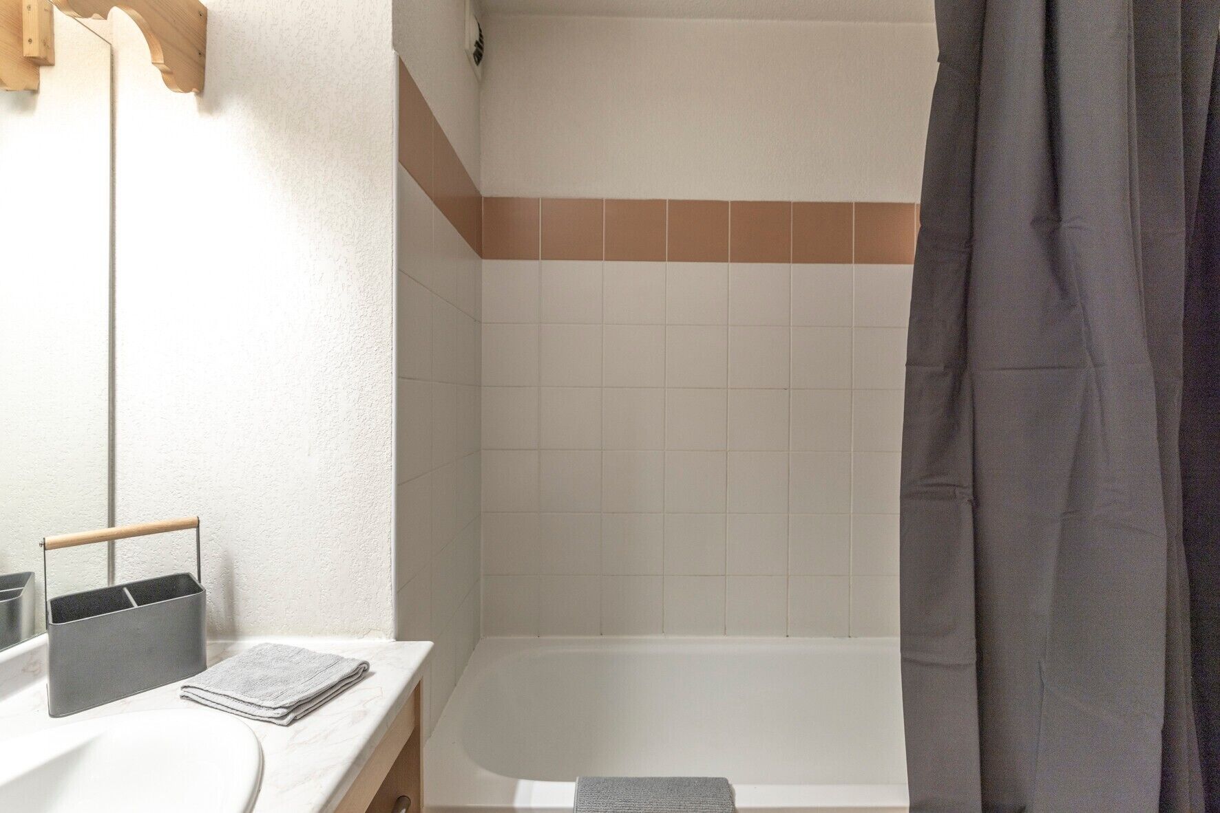 A bathroom with a white bathtub, a wooden towel rack, and a towel on the counter.