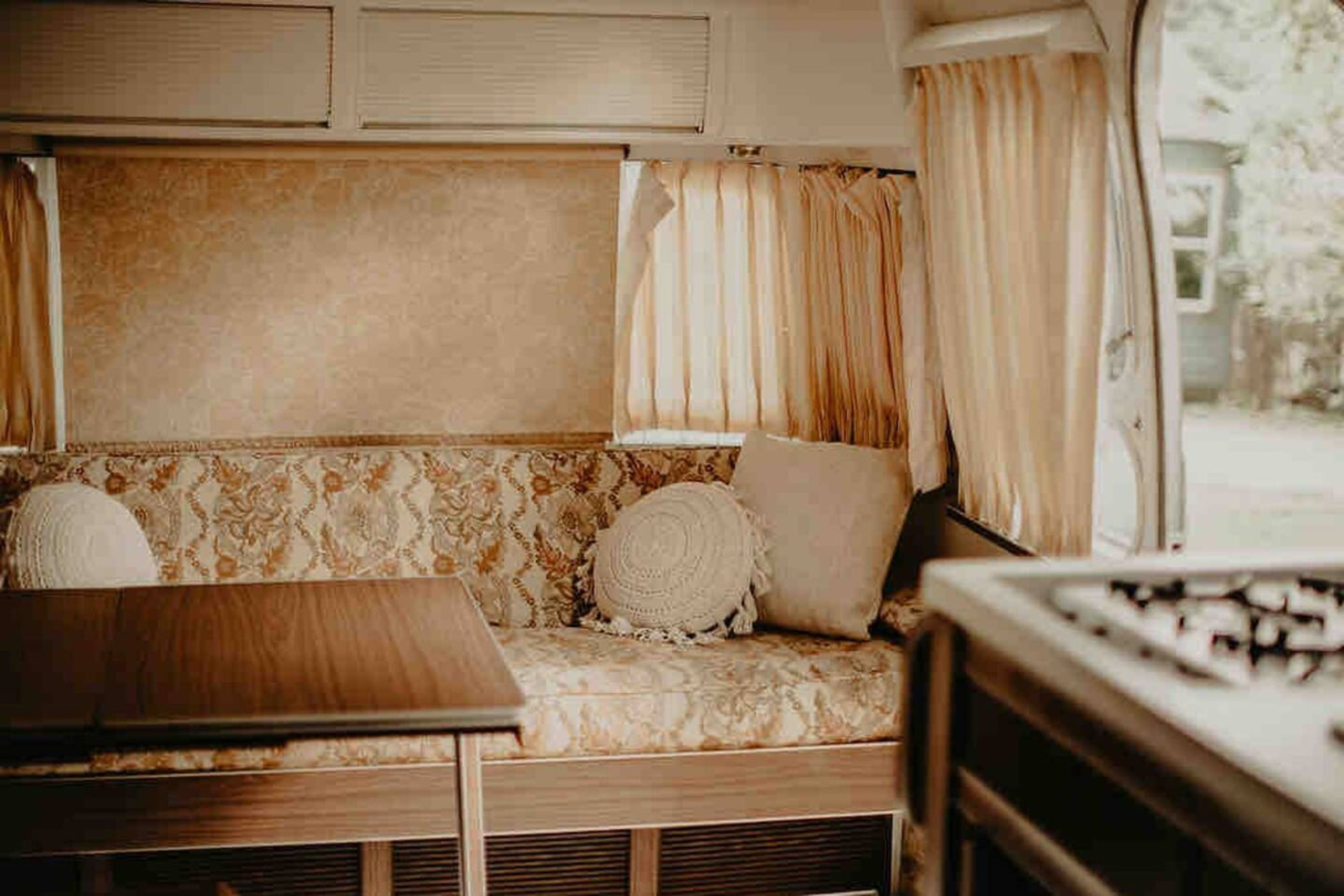 A cozy RV interior with a cushioned seating area, a wooden table, and curtains.