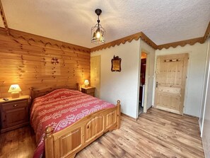 A wooden-paneled bedroom with a bed, nightstands, a wall clock, and a door.