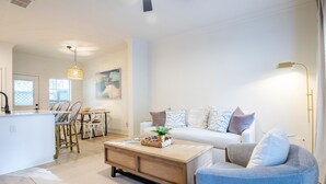 Un salon moderne avec un canapé blanc, un fauteuil bleu, une table basse en bois et un coin repas avec des chaises en osier.