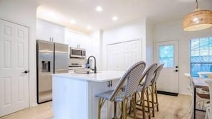 Une cuisine moderne avec des meubles blancs, un îlot central et un coin repas doté de chaises en osier.