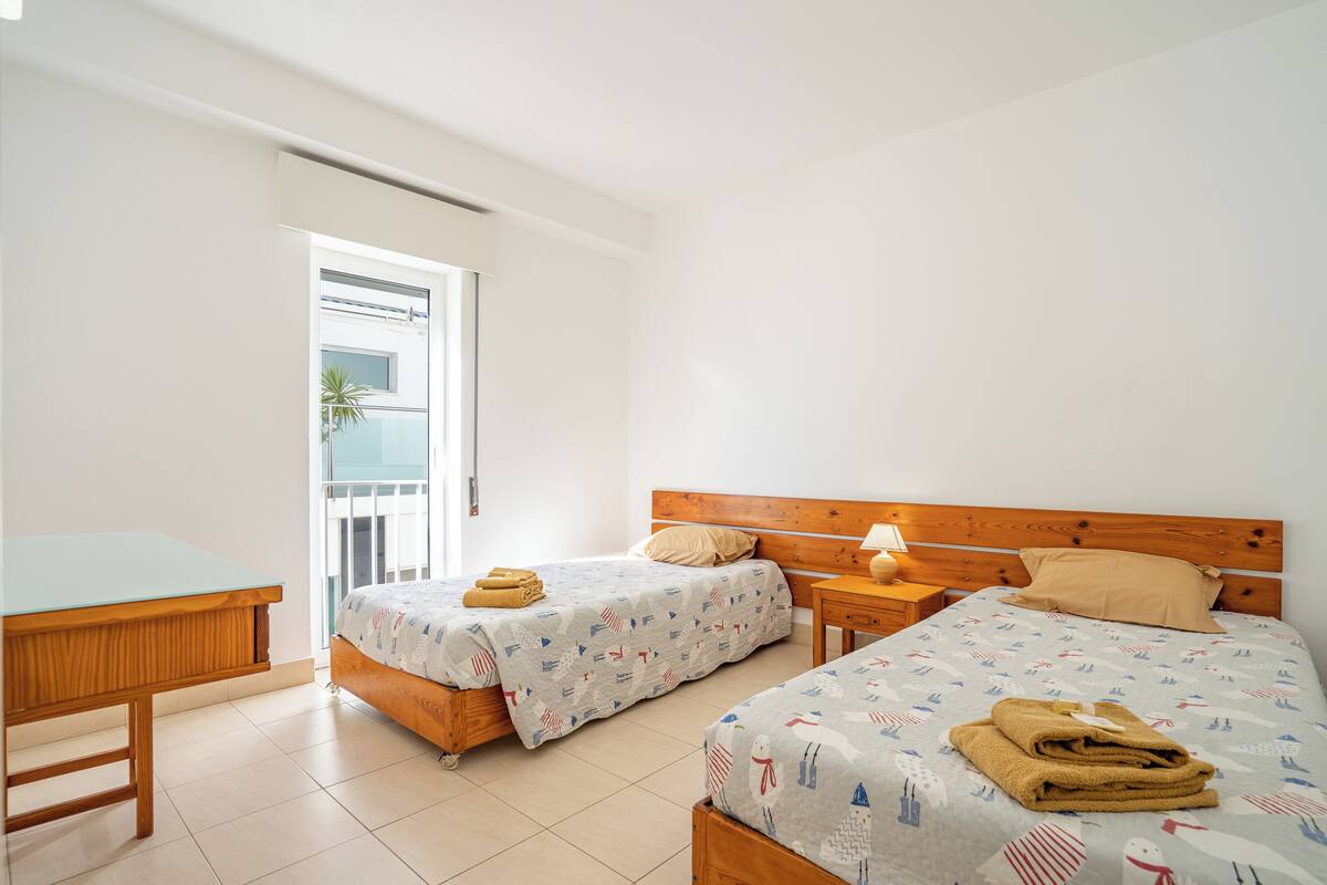 Habitación de hotel con dos camas, un escritorio de madera y un balcón.
