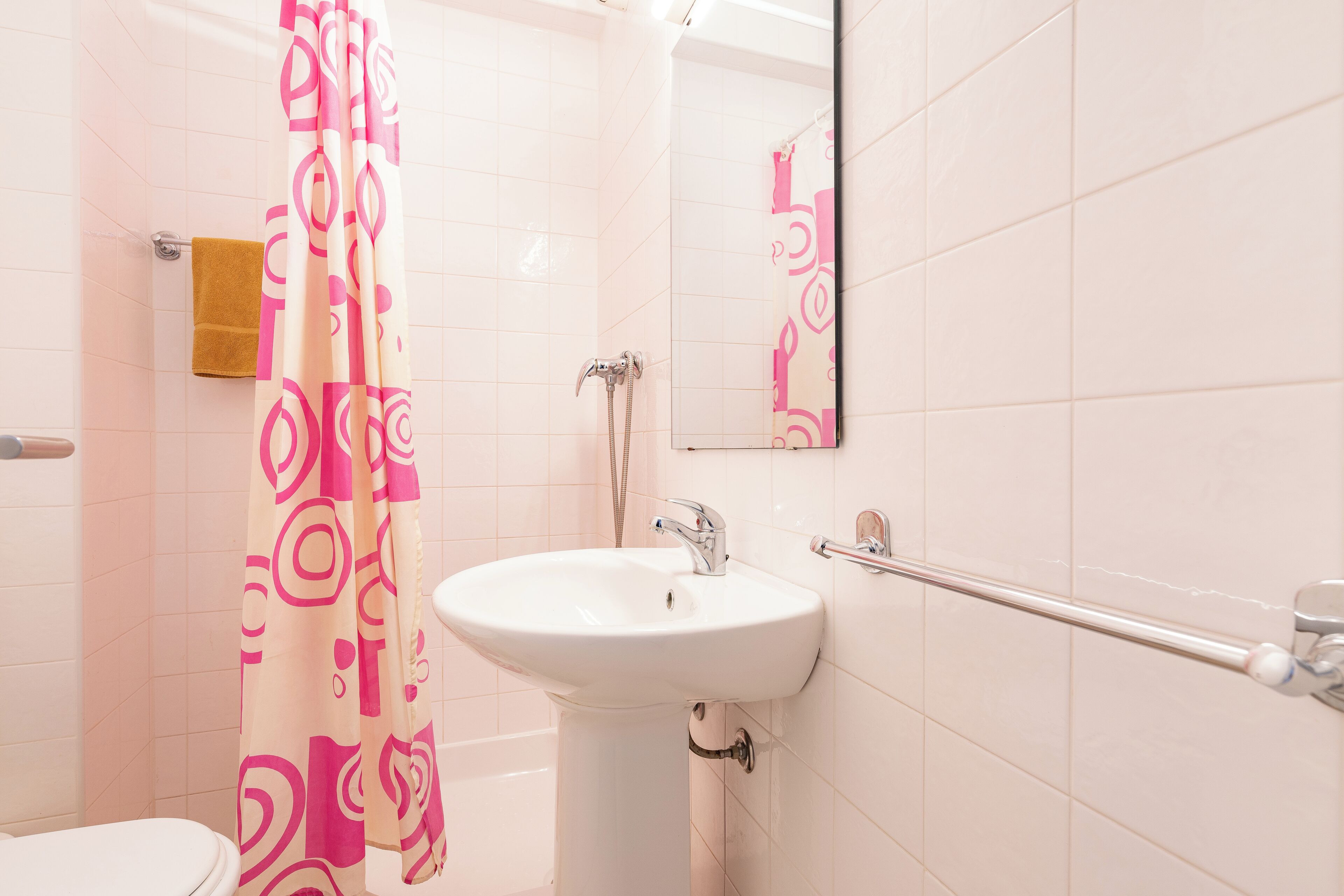 A bathroom with a white sink, a shower with a pink and white patterned shower curtain, and a towel rack with a brown towel.