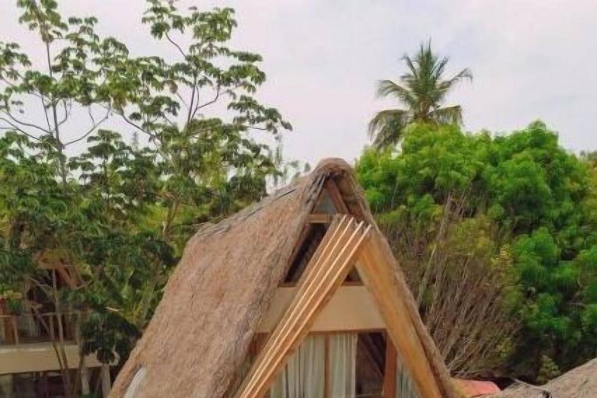 Una cabaña con techo de paja y balcón, rodeada de follaje tropical.