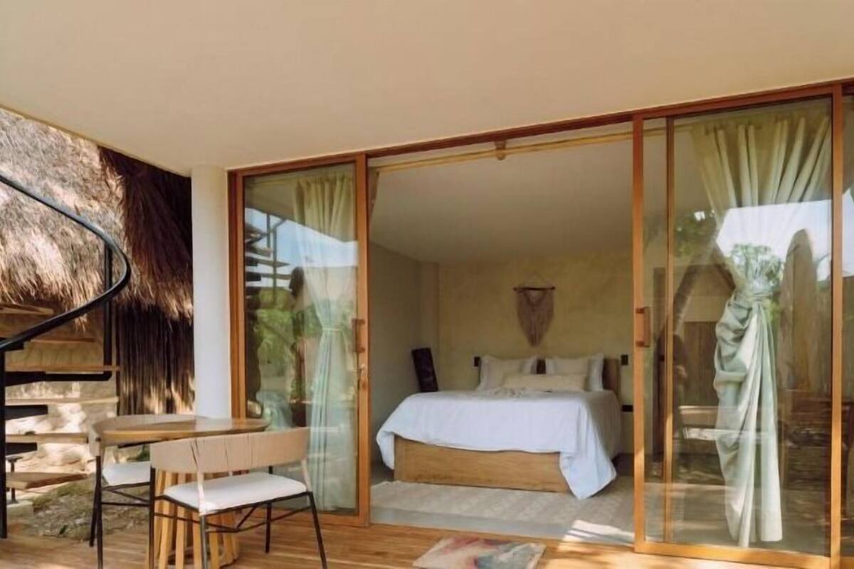 Un dormitorio con cama, escritorio y silla, y una puerta de vidrio que da a un espacio al aire libre.