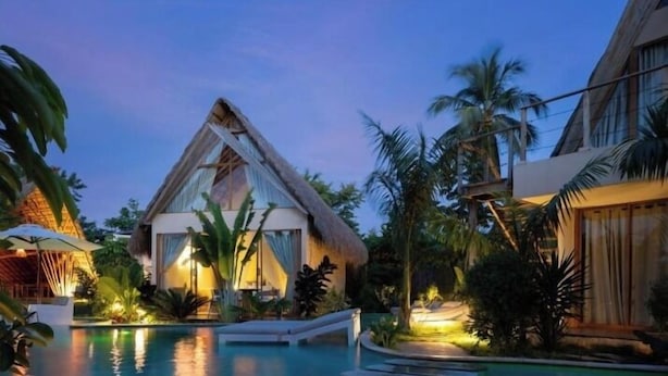 Un resort con piscina, palmeras y una construcción de techo de paja.