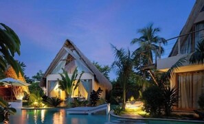 Un complexe hôtelier doté d’une piscine, de palmiers et d’un bâtiment à toit de chaume.