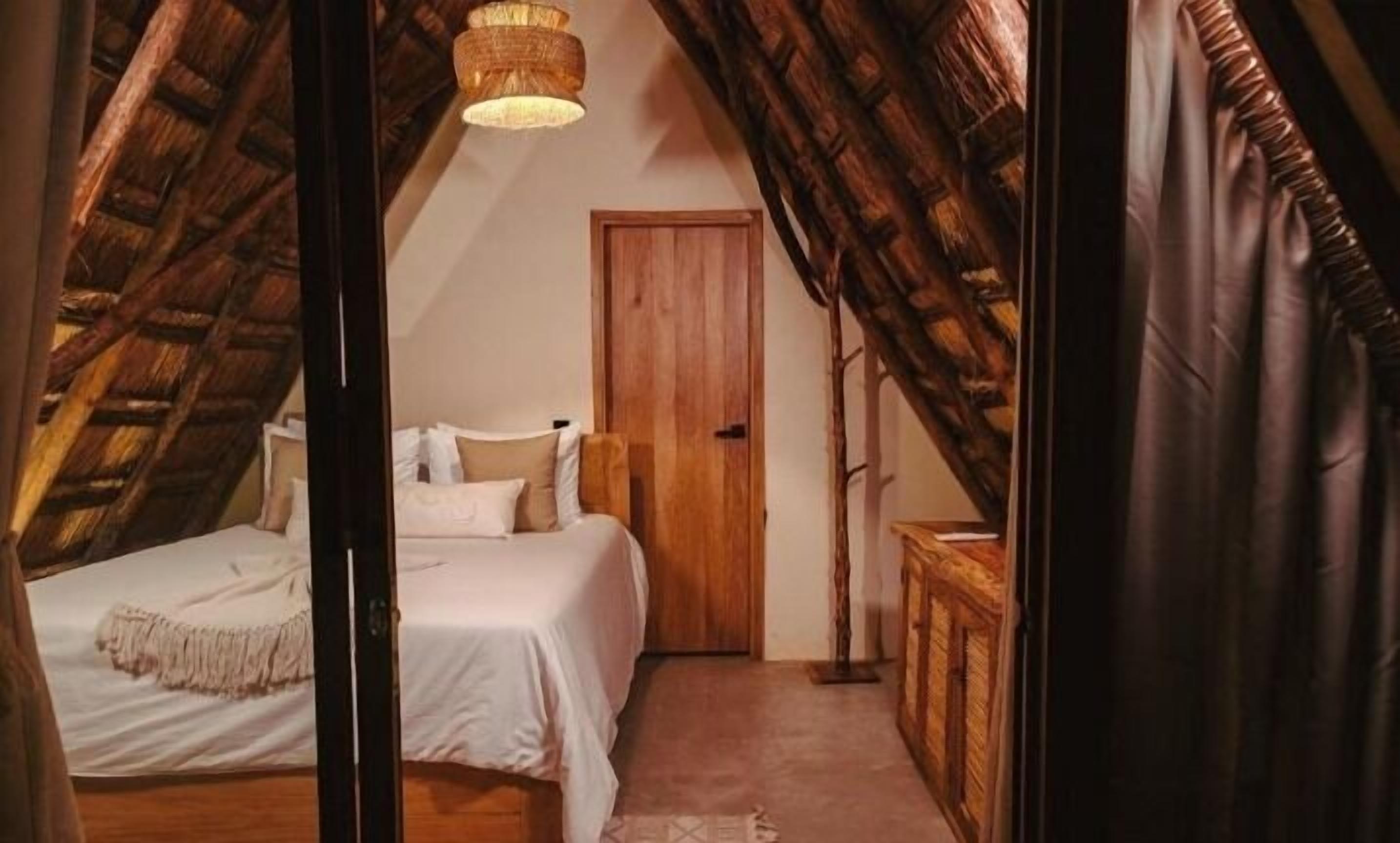 A bedroom with a sloped ceiling, a bed, a wooden wardrobe, and a door.