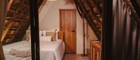 A bedroom with a sloped ceiling, a bed, a wooden wardrobe, and a door.
