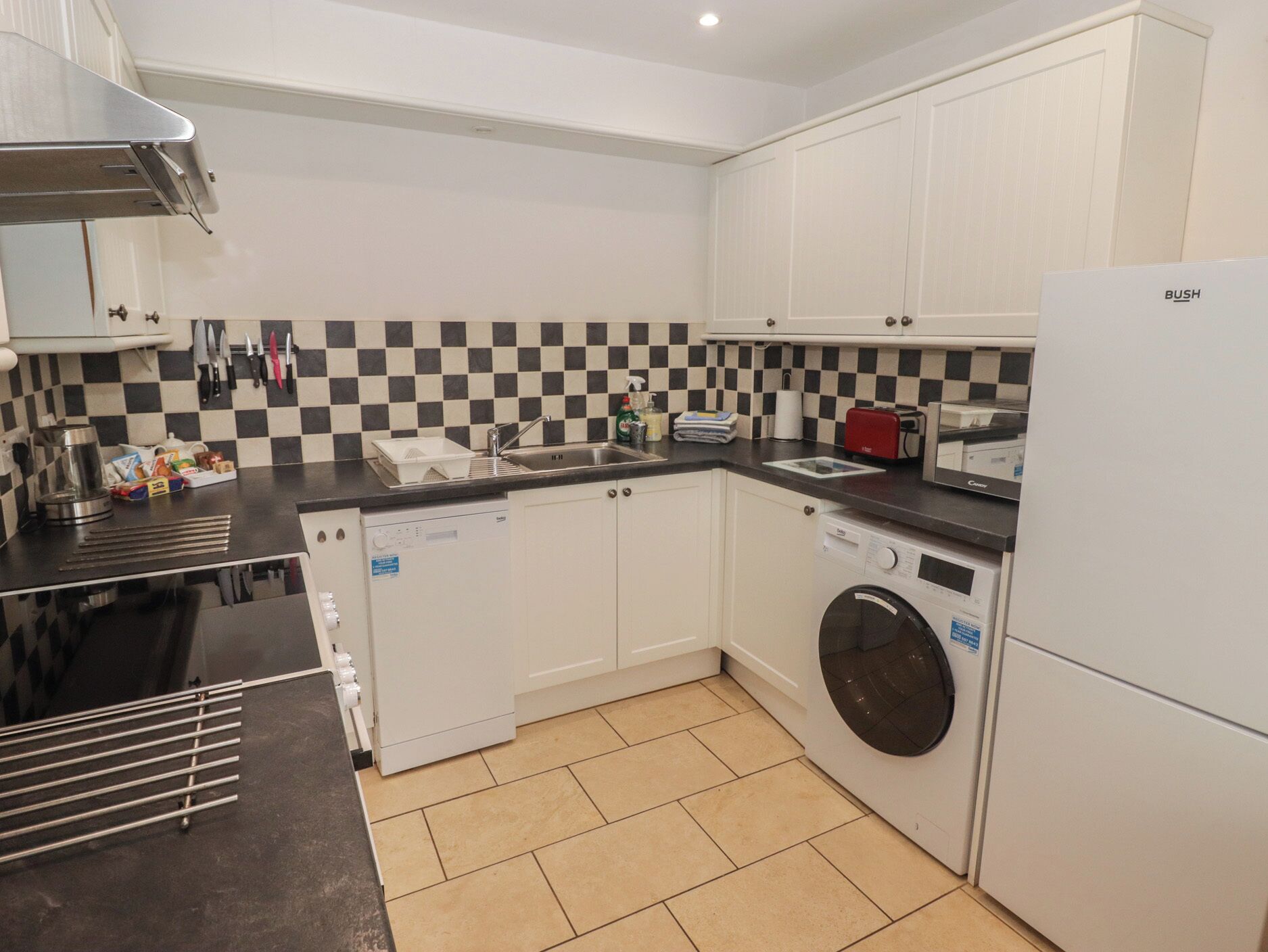 A compact kitchen with white cabinets, a black and white checkered backsplash, a dishwasher, a washing machine, and a refrigerator.
