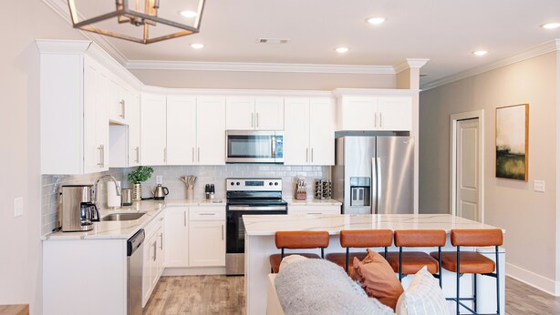 Una cocina moderna con armarios blancos, electrodomésticos de acero inoxidable y una isla central con taburetes de bar.