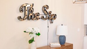 Una consola de madera con un jarrón de flores blancas, una lámpara y un adorno de pared.