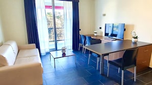 A modern living room with a sofa, a dining table with chairs, a TV, and a balcony with curtains. - Residence Roman (Pomezia)