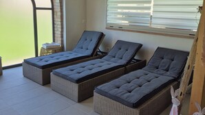 Uma sala de sol com três poltronas de vime, teto de madeira e uma grande janela em arco.