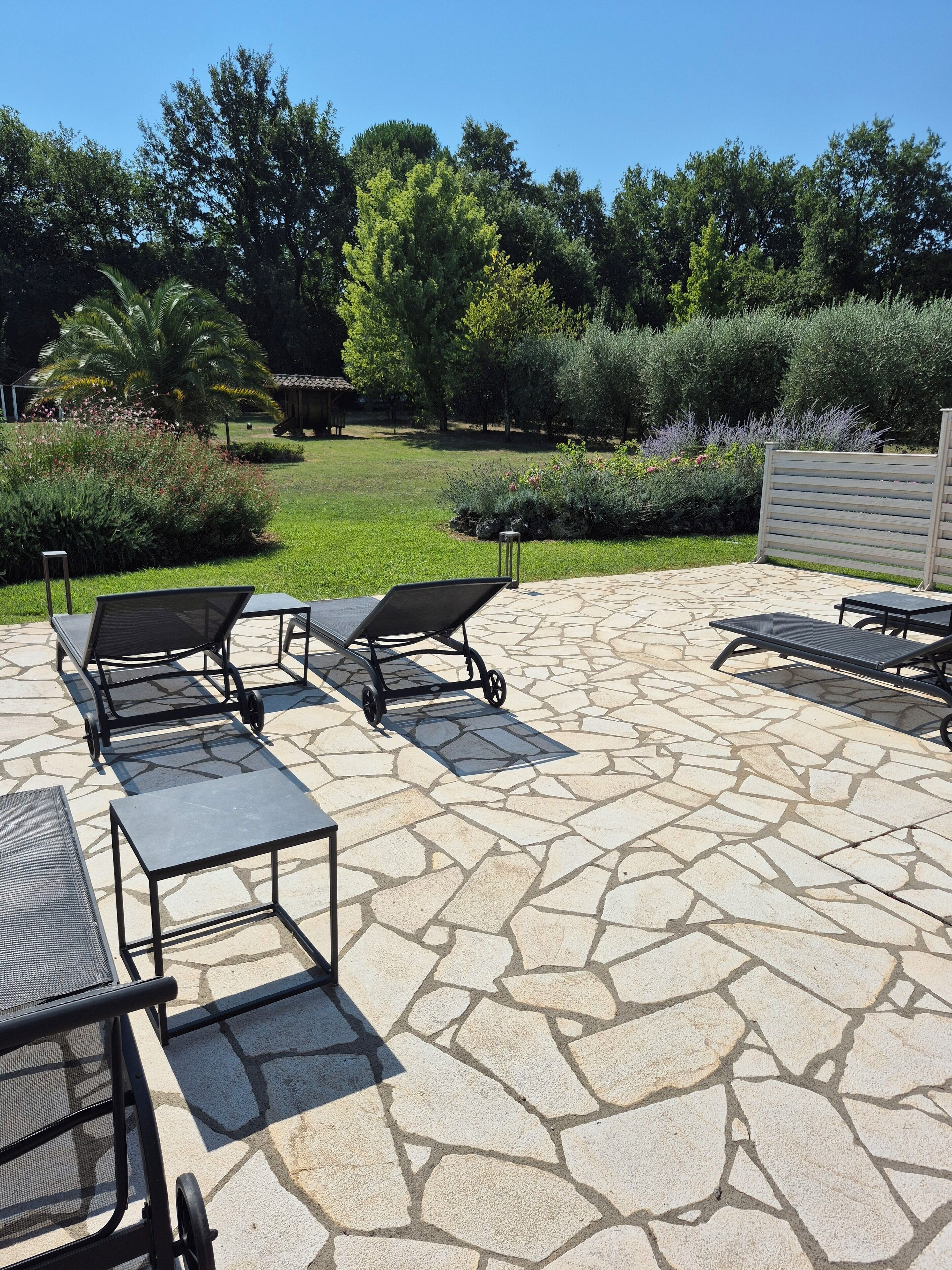 An outdoor patio with stone flooring, several lounge chairs, and a pergola structure.