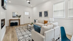 A modern living room with a sofa, coffee table, and a ceiling fan. - Modern Indy Retreat with Hot Tub, Outdoor Oasis, Prime location to Lucas Oil (Indianapolis)