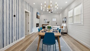 A dining area with a wooden table, blue chairs, and a chandelier. - Modern Indy Retreat with Hot Tub, Outdoor Oasis, Prime location to Lucas Oil (Indianapolis)