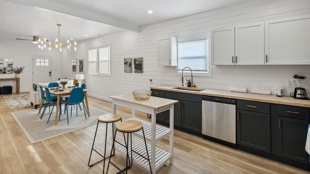 A modern kitchen with white cabinetry, a wooden countertop, and a dining area with blue chairs. - Modern Indy Retreat with Hot Tub, Outdoor Oasis, Prime location to Lucas Oil (Indianapolis)