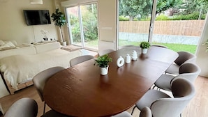 Un espace repas moderne avec une table ronde en bois, des chaises à revêtement gris et une grande fenêtre donnant sur un jardin.