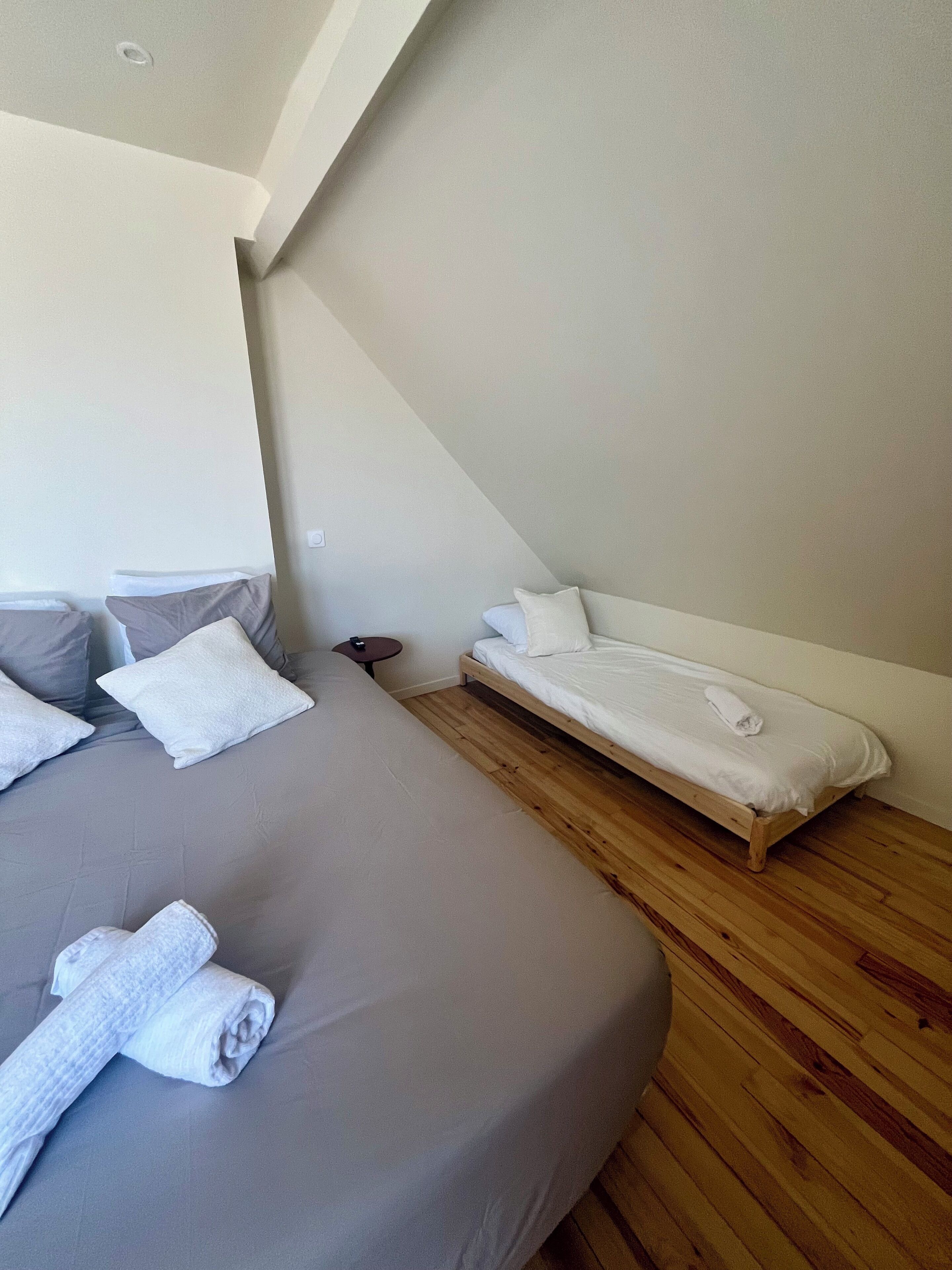 A bedroom with a large bed, a smaller bed, and a wooden floor.
