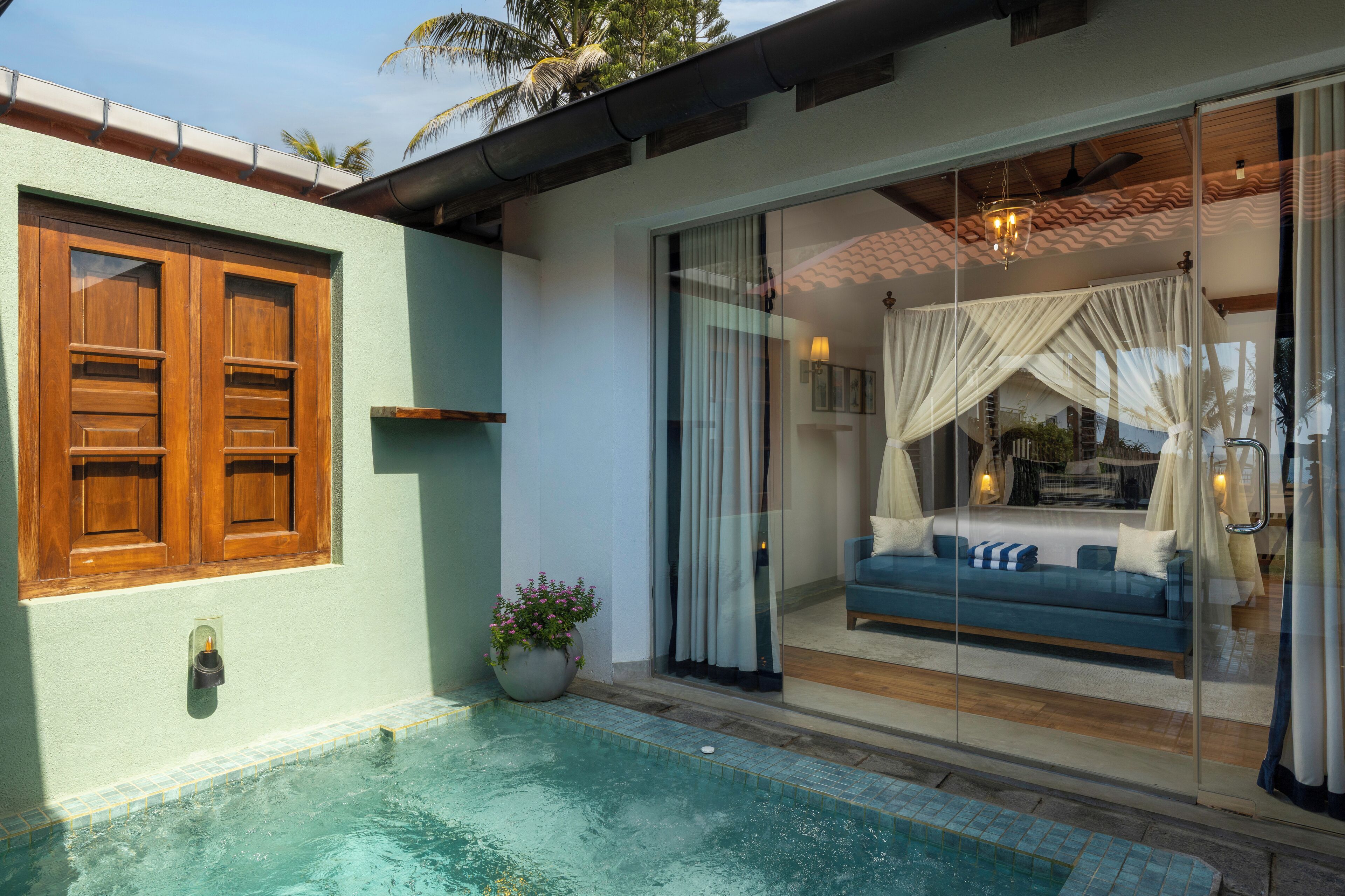 Un área junto a la piscina con un ventanal que da a una habitación con sofá azul y cortinas blancas.