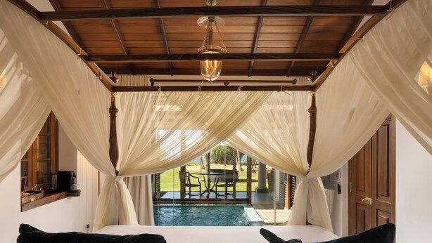 A bedroom with a canopy bed, a view of a swimming pool, and a wooden ceiling. - Oruva Beachside Villa (Galle)