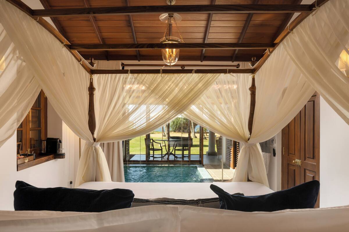 Une chambre avec un lit à baldaquin, une vue sur une piscine et un plafond en bois.