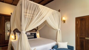 A bedroom with a four-poster canopy bed, bedside lamps, a blue sofa with a striped cushion, and wooden furniture. - Oruva Beachside Villa (Galle)