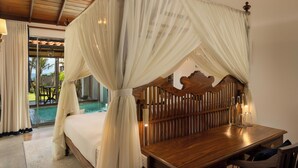 A bedroom with a four-poster canopy bed, wooden headboard, bedside table with bottles, and a view of an outdoor pool area. - Oruva Beachside Villa (Galle)
