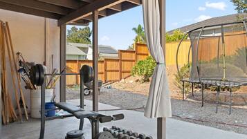 A covered outdoor gym area with exercise equipment, a trampoline, and a wooden fence in the background.