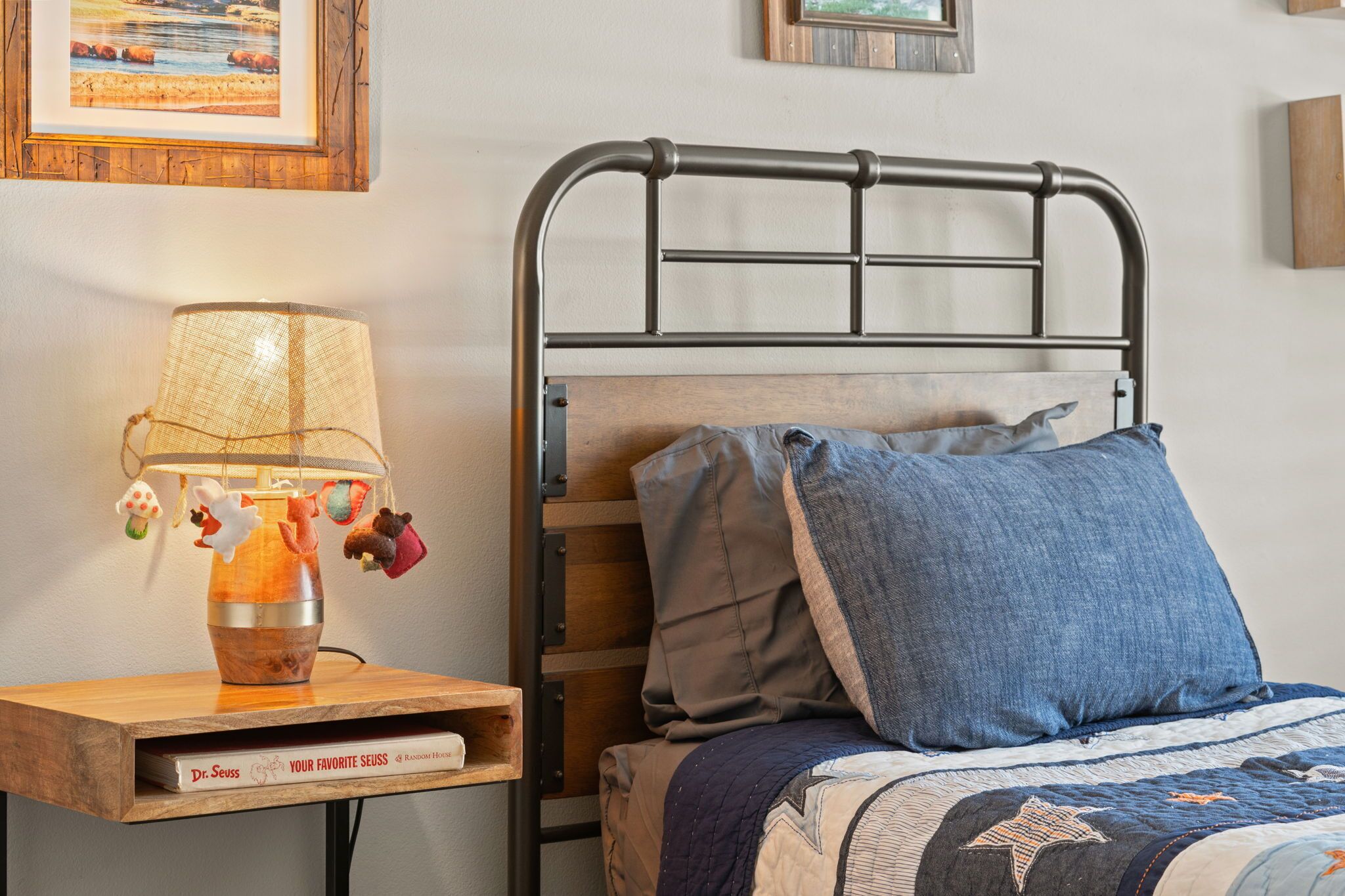 Un lit avec une tête de lit en métal, une table de chevet en bois avec une lampe et un livre intitulé « Le Dr. Seuss ».