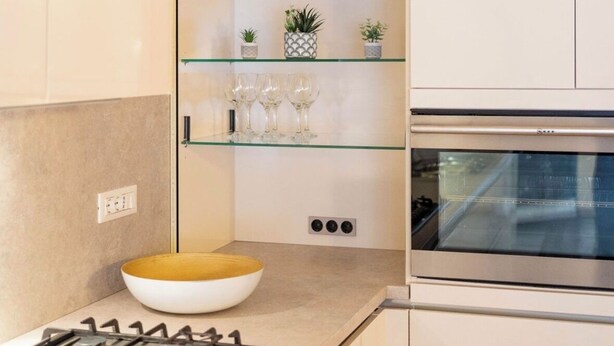 Une cuisine moderne équipée d’une cuisinière à gaz, d’un four encastré et d’une étagère en verre où sont exposés des objets décoratifs.