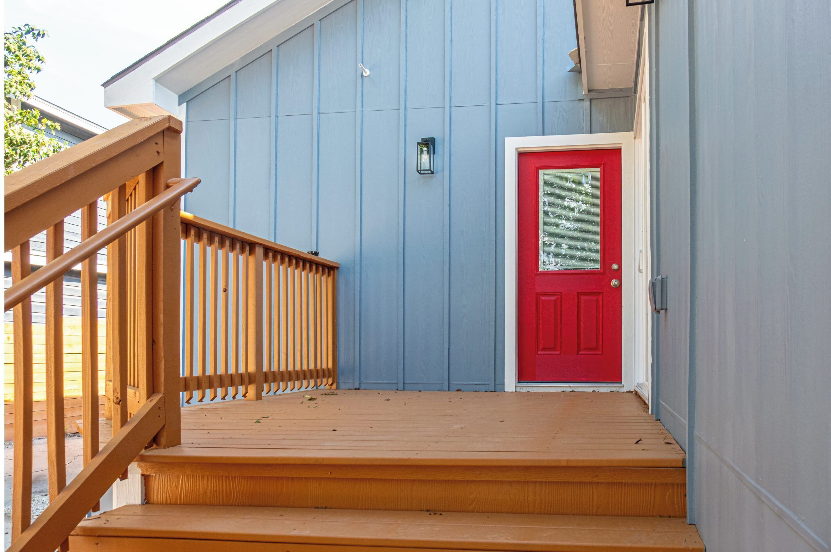 A wooden staircase leading to a red door, with a blue exterior wall and a small lantern above the door.