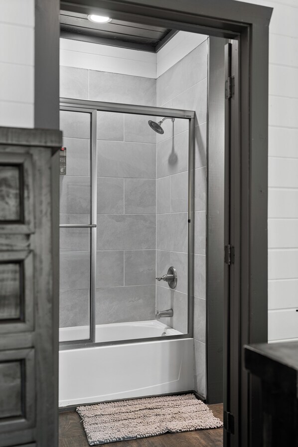 A modern bathroom with a glass-enclosed shower, a bathtub, and a wooden floor.