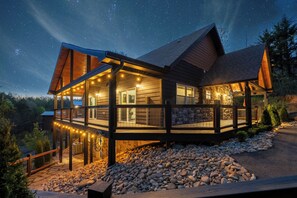 A modern cabin with a wooden exterior, large windows, and a deck with string lights.