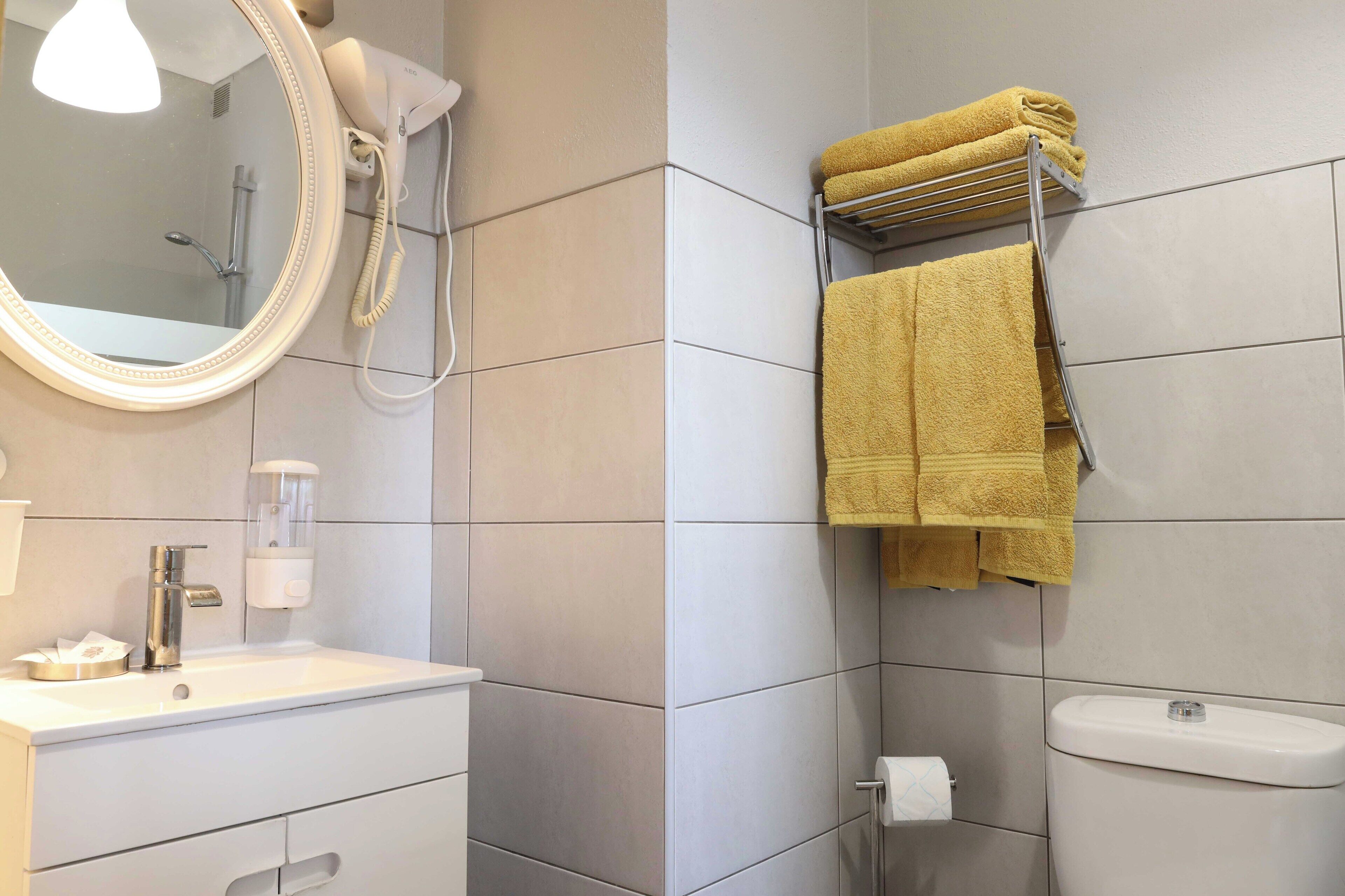 A bathroom with a white sink, a mirror, a towel rack with yellow towels, a toilet, and a shower.
