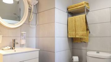 A bathroom with a white sink, a mirror, a towel rack with yellow towels, a toilet, and a shower.