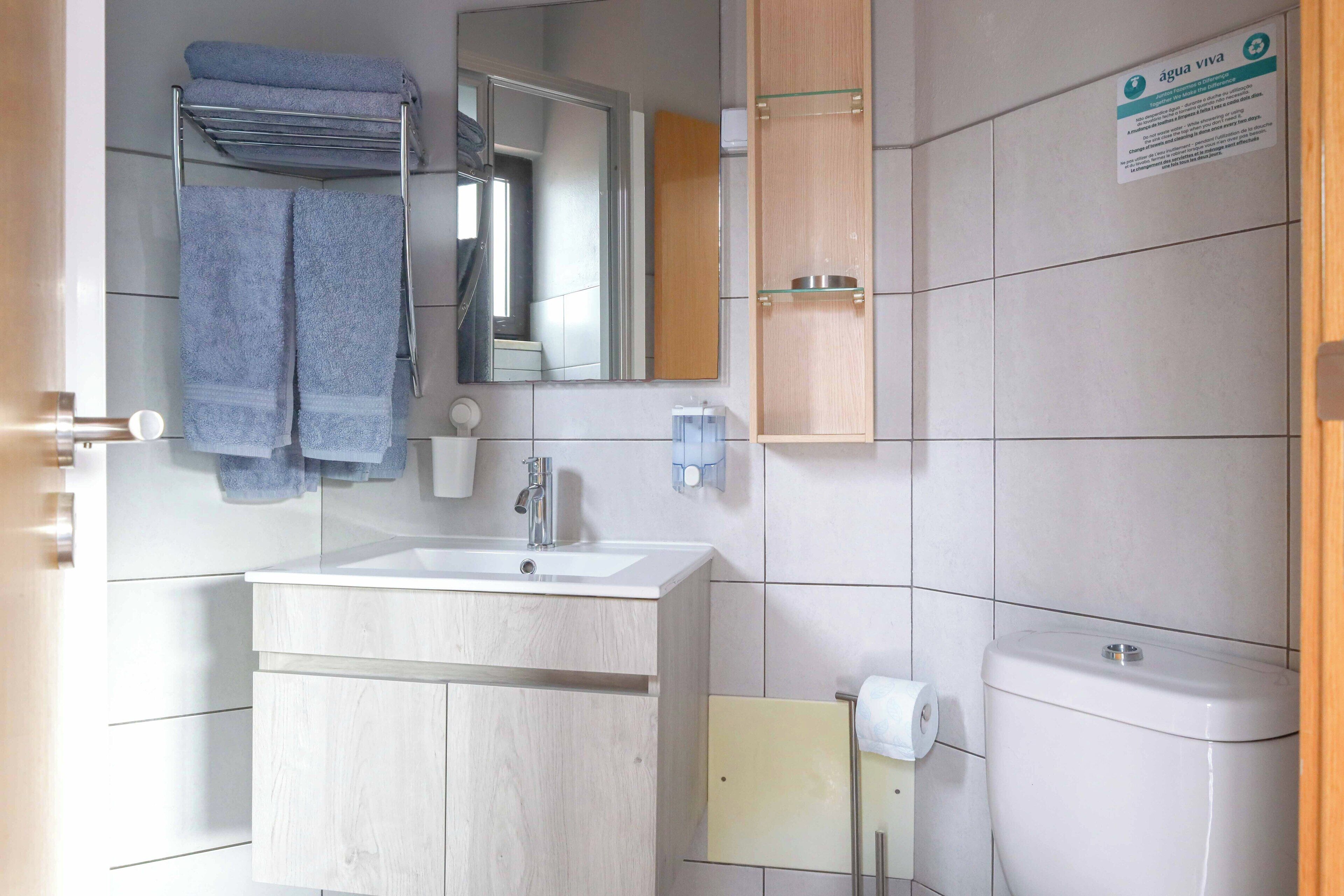 Een badkamer met een wastafel, spiegel, handdoekhouder en toilet.
