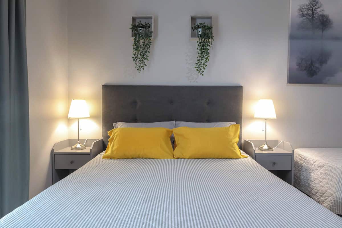 Ein Hotelzimmer mit einem großen Bett, zwei Nachttischlampen, einem Kopfteil und zwei Wandpflanzgefäßen.