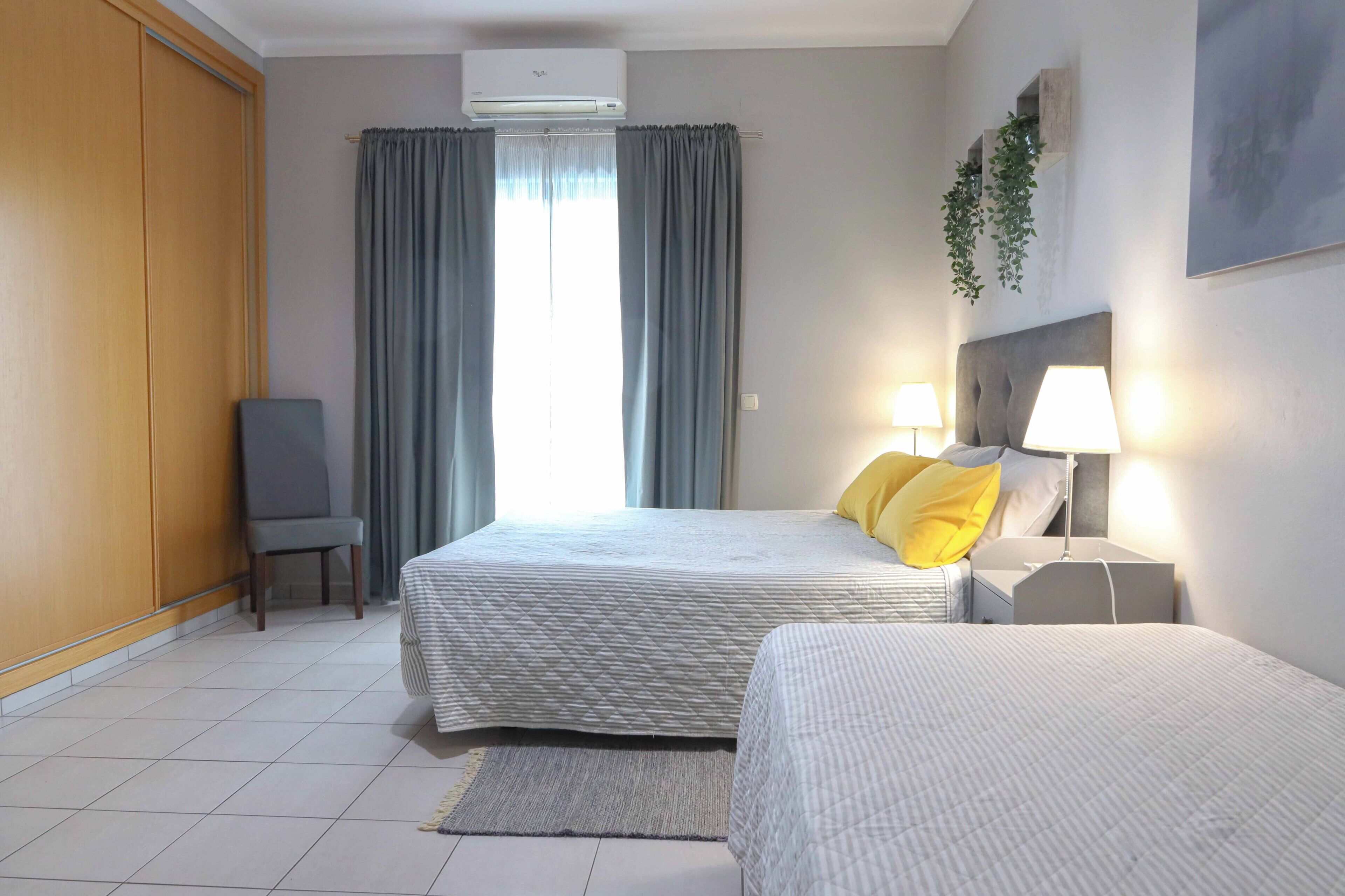 A hotel room with two beds, a chair, a desk, and a window with curtains.