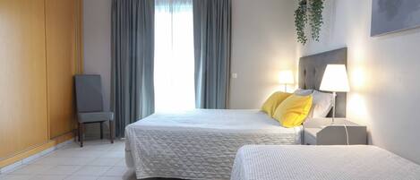 A hotel room with two beds, a chair, a desk, and a window with curtains.