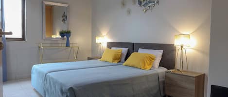Une chambre avec deux lits, des lampes de chevet, une table de chevet, une commode, un miroir et des œuvres d’art décoratives au mur.