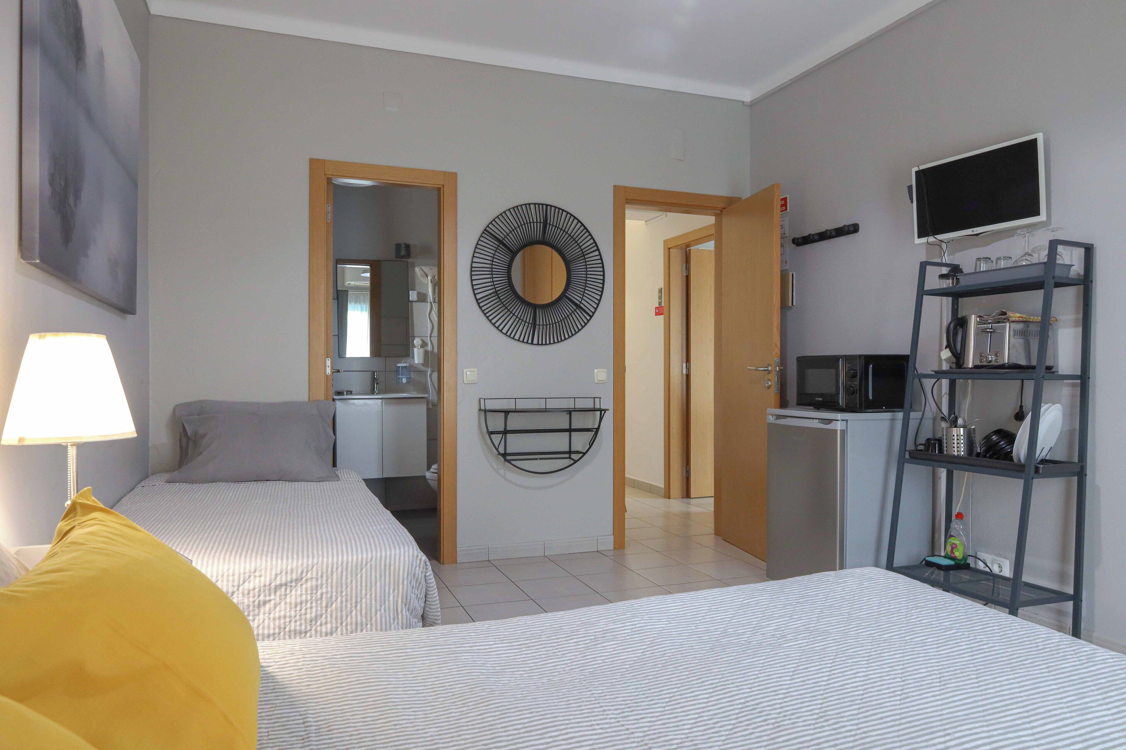 A hotel room with two beds, a desk, a TV, and a kitchenette.