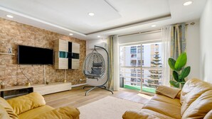 Una sala de estar con sofá, una silla colgante, televisor y un ventanal con vistas a edificios.