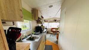 Eine kleine Küche mit Spüle, Arbeitsplatte und Holzschränken. Ein Fenster sorgt für natürliches Licht und bietet einen Ausblick ins Freie.
