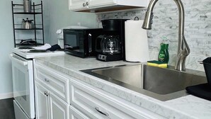 A modern kitchen with white cabinetry, a stainless steel sink, and a marble backsplash. - Centrally + Conveniently Located (Providence)
